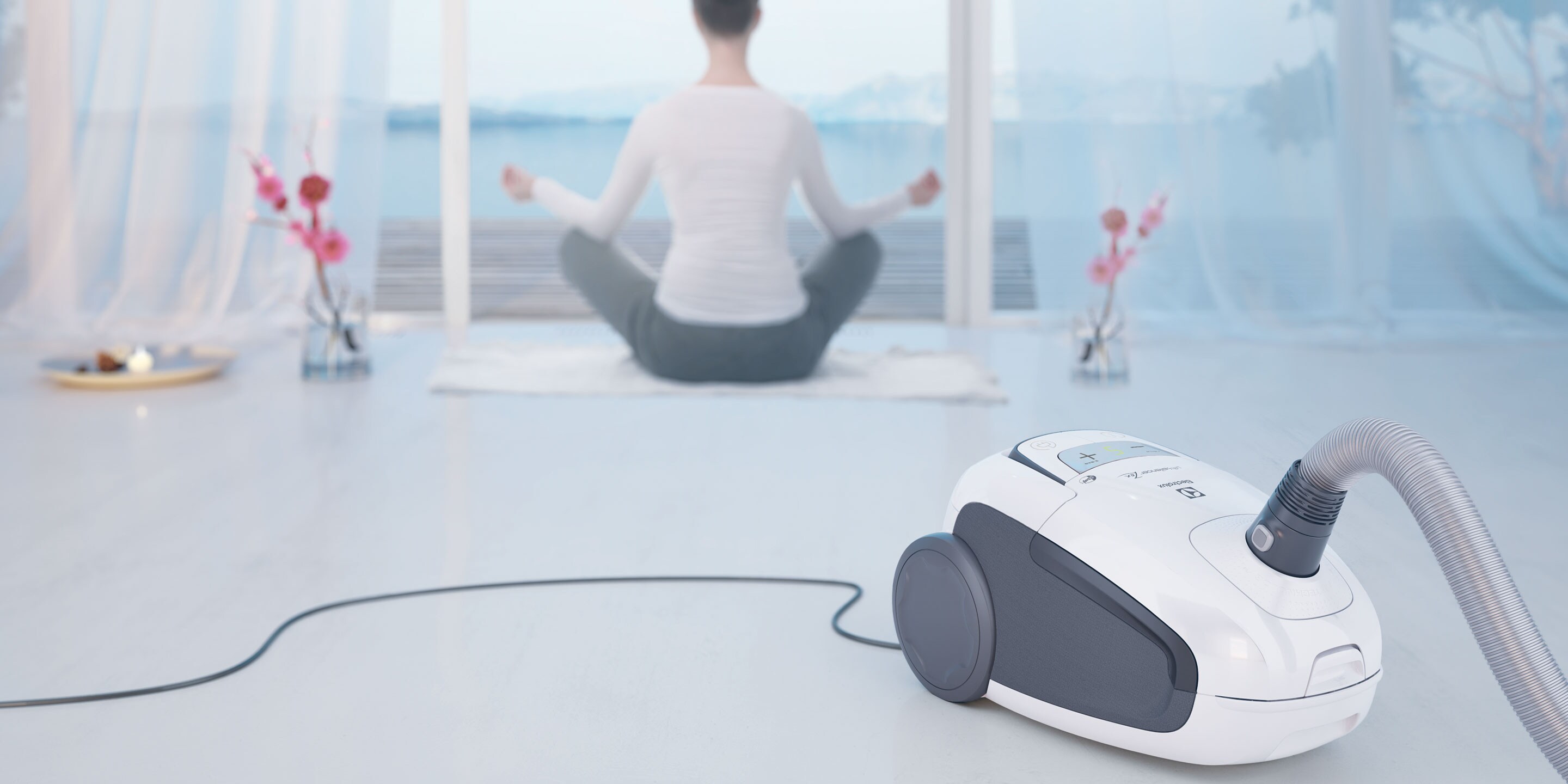 Žena cvičící jógu s vysavačem Electrolux Ultra Silencer v popředí