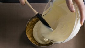 Cukrář lije hladkou směs pro tvarohový dort do kulaté formy, která je tak připravena do trouby
