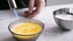 Pekař karamelizuje cukr na crème brûlée pomocí kuchyňského plamenometu