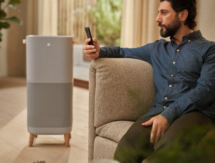 Muž sedící u čističky vzduchu a držící telefon.