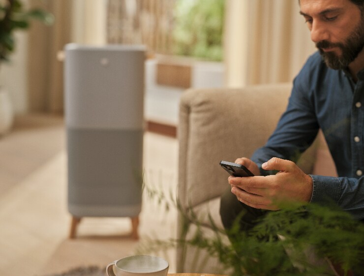 Muž sedící u čističky vzduchu a držící telefon.