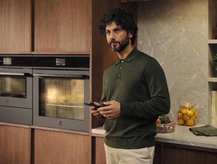 Muž stojí v kuchyni a drží telefon.