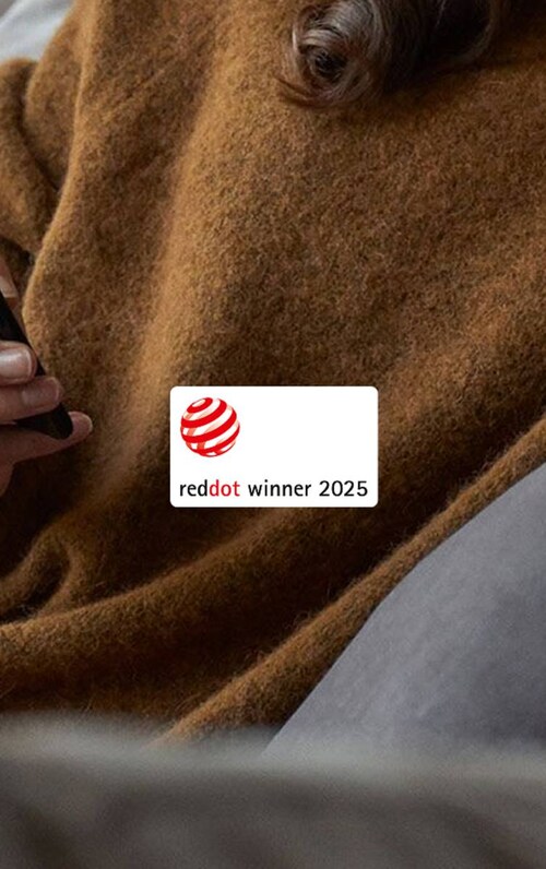 Žena v vlněném svetru sedí na pohovce s mobilem. Na obrázku je logo Red Dot Design.