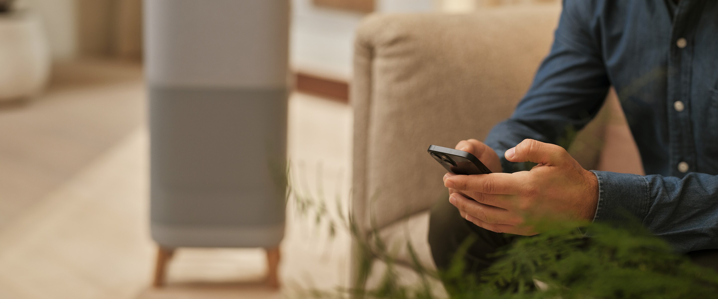 Muž sedí a drží telefon. V pozadí je čistička vzduchu.